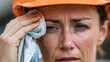 © Oleksandr - Close-up portrait of a hardworking woman in an orange safety helmet, her brow furrowed in concentration, wiping excessive sweat from her face during strenuous outdoor labor