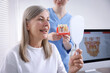© New Africa - Woman looking at her teeth in mirror and doctor with dental implant model in clinic, closeup