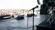 © Xenia - Microphone on a stand on an outdoor concert stage facing a blurred crowd. Live music festival and summer entertainment concept