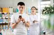 © JackF - In sales area of pharmacy, guy examines packaging of antitussive syrup, reads characteristics and properties, checks expiration date and storage conditions. Pharmacist offer similar product item