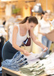 © JackF - Young woman stands near denim clothes and chooses pants and shorts made of high-quality denim. European woman shopping in summer