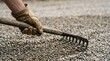 © SimpleDesignStudio - Worker spreading gravel with a rake for landscaping project, close up of gloved hand leveling crushed stone for driveway construction