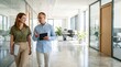 © ameliabusinessstock - Two professionals walking and reviewing tablet documents in bright modern office corridor