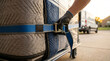 © ViskBx - Closeup of a mover securing a large furniture item wrapped in moving blankets and plastic wrap with a heavyduty ratchet strap