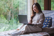 © Farknot Architect - Portrait of a woman using and working on laptop computer while sitting on bed at home