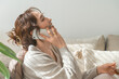 © buritora - A stylish woman sitting on a sofa and talking on her smartphone.