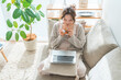 © buritora - A woman sitting on a sofa, sipping tea and looking at her computer.