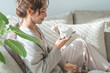 © buritora - An Asian woman sitting on the living room sofa, looking at her smartphone.