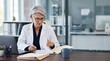 © Eve - Mature senior woman doctor physician in white medical uniform reviewing patient medical history records documentation file at desk with laptop in hospital office clinical concept