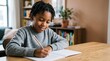 © Eve - Smiling African American schoolboy writing with pencil in notebook at desk. Diligent black child student studying at home, early development and education.