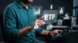 © umi - ETF Investment Concept: A man in a teal shirt uses a tablet and gestures towards a holographic display showing ETF along with financial icons, symbolizing investment and trading.