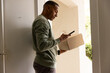 © Wavebreak Media - African American man standing at front door wearing green sweater holding box while using phone