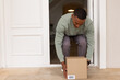 © Wavebreak Media - African American man crouching and lifting cardboard shipping box at home entryway with wristwatch