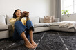 © Wavebreak Media - Adult African American woman sitting on rug by sofa holding mug wearing yellow top, copy space