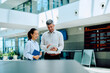© we.bond.creations - Two diverse colleagues collaborating and reviewing information on a tablet in a contemporary office lobby or airport terminal