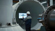 © stefanholm - An engineer stands inside a giant, hollow wind-turbine base, monitoring a monitor showing a pulse-wave of gear vibrational health data.
