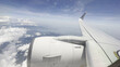 © Baljeet - High angle aerial view of an airplane wing and engine flying above white clouds under a blue sky