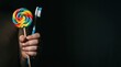 © 24DIY - Close up of a hand holding a colorful swirl lollipop and a blue toothbrush