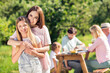 © deagreez - Mother hugging daughter at a sunny family picnic with relatives enjoying an outdoor meal and relaxed multigenerational gathering