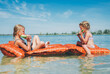 © Soloviova Liudmyla - two young girls eating watermelon slices while relaxing on orange inflatable float mattress in lake water during sunny summer vacation representing childhood freedom friendship and outdoor leisure