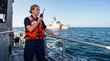 © Xenia - Female Coast Guard officer using a radio on a boat. Woman in orange life jacket on duty at sea. US Coast Guard Day concept