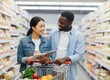 © KIMOG - Happy African American Man Looking at Asian Woman Holding Notebook While Grocery Shopping