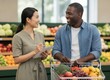 © KIMOG - Happy African American Man Looking at Asian Woman Holding Notebook While Grocery Shopping