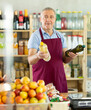 © JackF - Elderly male seller at counter offering olive or sunflower oil in bottle in grocery store