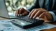 © btiger - Focused hands using a calculator on financial charts with laptop in background conveying concentration and professionalism