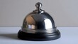 © Mariya - Shiny chrome service bell on a black round base resting on a neutral countertop, polished reflections conveying a welcoming and professional hotel reception mood