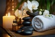 © Hal - rolled white towel, stacked black massage stones and smooth pebbles, delicate white orchid blossoms, small oil bottle and glowing candle on a bamboo mat creating a calm relaxing spa atmosphere
