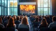 © tiger - Attentive audience listening to a panel of four speakers on stage in a sunlit modern conference hall with large glass windows and a glowing presentation screen