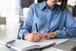© fizkes - Closeup cropped view of business woman, office employee writing notes in planner, organizes tasks, outlines ideas, updates schedules, and prepares project details, working at modern desk with laptop