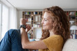 © Westend61 - Smiling woman at home sitting on couch looking at smartwatch