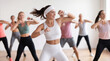 © ChaoticDesignStudio - Athletic woman leading high-energy cardio dance class in bright fitness studio. Group of diverse people following choreography during aerobic workout session.