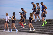 © master1305 - Mixed running club going down stone steps after outdoor training session. Concept of recovery pace, team fitness, urban cardio, endurance practice and healthy active lifestyle.