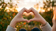 © Rizwan Akbar - Two hands shaping a heart symbol against a warm, sunlit golden hour nature background filled with soft bokeh.