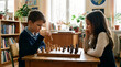 © Natalia - Children thinking intensely while playing chess in a bright classroom