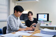 © Stella 16 - Two business professionals are reviewing documents and discussing a project, collaborating effectively at a conference table with laptops and papers in a contemporary corporate office setting