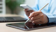 © Father_Studio - Businesswoman using a stylus pen on a digital tablet while holding a smartphone, representing electronic signatures, digital documentation, paperless workflows, business technology, and productivity.