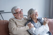 © luciano - Happy senior couple is sitting on a sofa, embracing and laughing with eyeglasses, experiencing genuine joy and connection in their retirement years