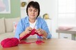 © New Africa - Senior woman knitting with needles at wooden table indoors, space for text