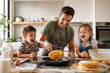 © warleysoares - Pai e filhos pequenos fazendo panquecas juntos em uma cozinha ensolarada - Conceito de diversão em família, café da manhã especial e amor paterno.