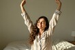 © Oleksandr - Young woman in striped pajamas stretches happily in bed. Sunlight streams into her room as she wakes up feeling refreshed and energized. She embraces the start of a new day with a joyful expression.