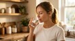 © Masque - A woman with light brown hair drinking a glass of water in a warm kitchen.