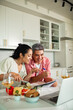 © Marko Geber - Smiling couple taking online cooking class in home kitchen