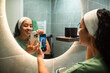 © Marko Geber - Woman brushing teeth and taking selfie in modern bathroom mirror