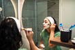 © Marko Geber - Woman applying facial mask in home bathroom mirror
