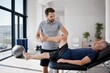 © Studio - Professional male physiotherapist stretching leg of senior patient on massage table in bright modern rehabilitation clinic, focused healthcare and physical therapy concept