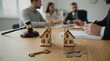 © Varos - A legal professional meeting with a couple regarding a property division, illustrated with two small house models, a paper couple figure, a key, and coins on a wooden desk.